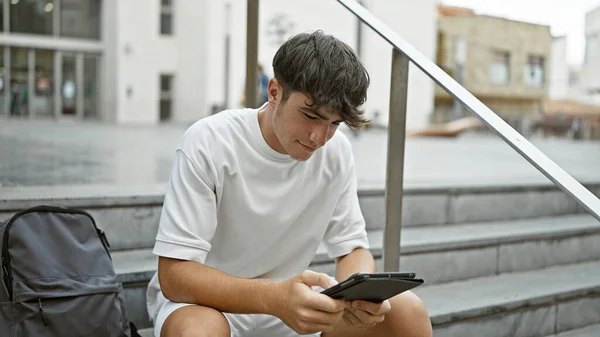 クールな若いヒスパニック系のティーンエイジャー 真剣な学生 気軽に大学の階段に座って 彼のラップトップスクリーンに囲まれて タッチパッドに集中 屋外でスマートテクノロジーライフスタイルを体現 — ストック写真