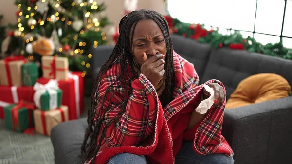 African woman feeling sick sitting on the sofa by christmas tree at home