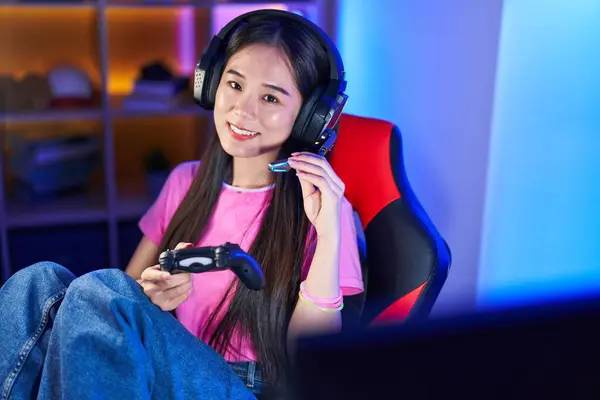 Young chinese woman streamer playing video game using joystick at gaming room