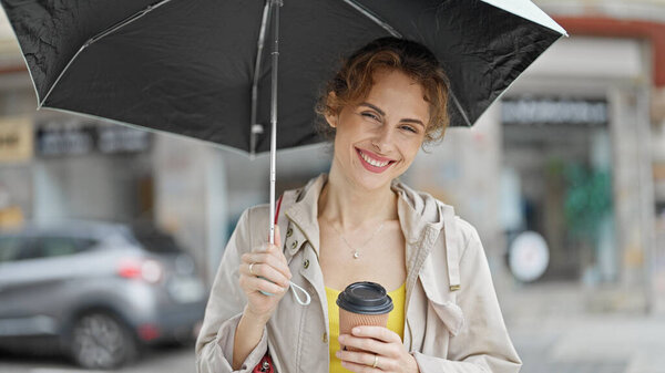Young woman holding umbrella and coffee smiling at street