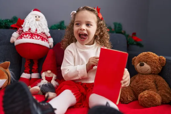 自宅でクリスマスの装飾でソファーに座っている愛らしいブロンドの少女の読書本 — ストック写真
