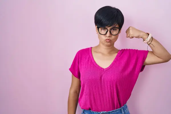 年轻的亚洲女人 短发耸立在粉红的背景上 强壮的人显示出臂膀肌肉 自信而自豪 — 图库照片