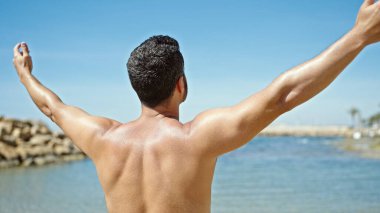 Genç İspanyol turist plajda kollarını açmış üstsüz duruyor.