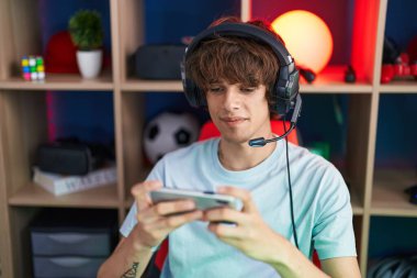 Genç sarışın adam oyun odasında akıllı telefon kullanarak video oyunu oynuyor.