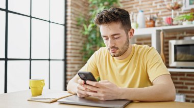 Genç İspanyol adam yemek masasında akıllı telefon kullanıyor.