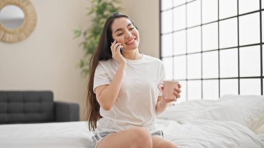 Genç, güzel, İspanyol bir kadın. Akıllı telefondan konuşuyor. Yatak odasında kahve içiyor.