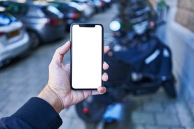 Akıllı telefon tutan adam motosiklet parkında beyaz beyaz ekran gösteriyor.