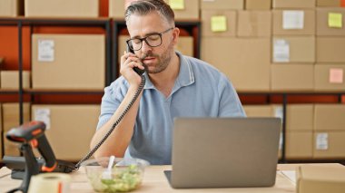 Gri saçlı bir adam telefonda konuşuyor ofiste salata yiyor.