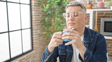 Kafkasyalı genç bir adam yemek odasındaki masada oturmuş kahve kokusu alıyor.