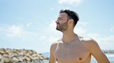 Genç İspanyol turist plajda üstsüz duruyor.