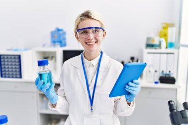 Genç sarışın bilim adamı laboratuarda dokunmatik yastık şişesi ve sıvı kullanıyor.