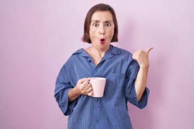 Orta yaşlı Latin bir kadın kahve içerken elleri yana dönük, ağzı açık şaşkın bir şekilde şaşırdı.. 