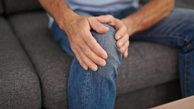 Orta yaşlı bir adam evinde dizinden sakatlanarak koltukta oturuyor.