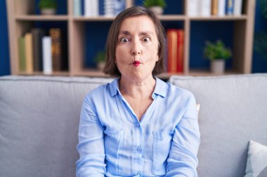 Orta yaşlı İspanyol bir kadın evinde kanepede oturup dudaklarıyla balık suratı yapıyor, çılgınca ve komik bir jest. Komik ifade. 