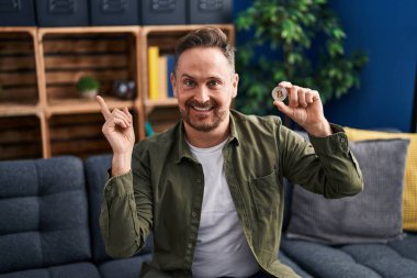 Orta yaşlı, beyaz bir adam elinde sanal para tutuyordu. Bitcoin gülümsüyordu. 