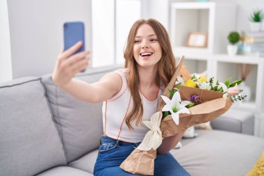 Beyaz çiçek buketi tutan beyaz bir kadın selfie çekerken gülümsüyor ve kahkahalarla gülüyor.. 