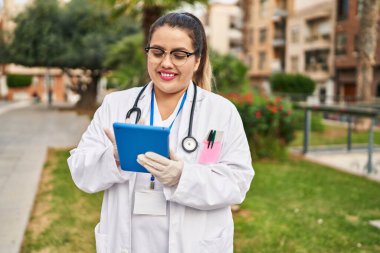 Young beautiful plus size woman doctor smiling confident using touchpad at park