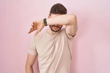 Sakallı İspanyol bir adam pembe arka planda dikiliyor. Gözleri kollarıyla kapatıyor, ciddi ve üzgün görünüyor. Görme, saklama ve reddetme konsepti 