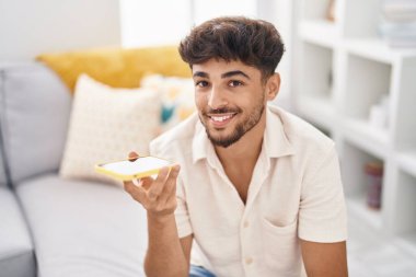 Young arab man talking on the smartphone sitting on sofa at home