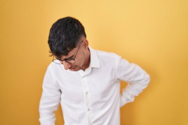 Sarı arka planda duran İspanyol genç adam sırt ağrısından muzdarip, elle dokunuyor, kas ağrısı 