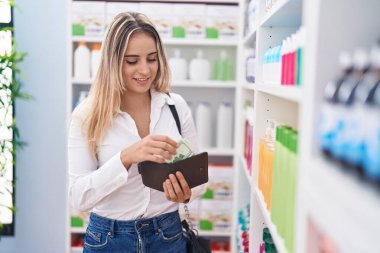 Genç sarışın müşteri gülümsüyor. Eczanede kendine güvenen bir cüzdan taşıyor.