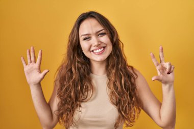 Sarı arka planda duran genç İspanyol kadın sekiz numaralı parmaklarıyla gülümseyerek kendinden emin ve mutlu bir şekilde işaret ediyor.. 