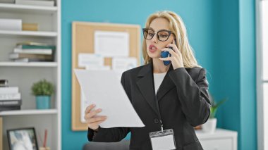 Genç sarışın iş kadını. Ofiste akıllı telefon okuyarak konuşuyor.