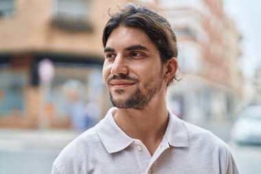 Young hispanic man smiling confident looking to the side at street