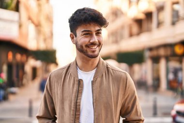 Young hispanic man smiling confident looking to the side at street