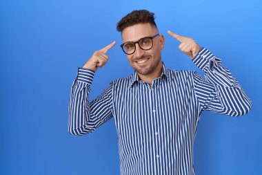 Sakallı, gözlüklü, gülümseyen, iki eliyle kafasını gösteren, harika bir fikir ya da düşünce, iyi bir hafıza. 