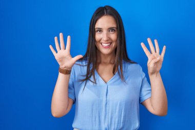 Mavi arka planda duran genç esmer kadın dokuz numaralı parmaklarıyla işaret ederken kendinden emin ve mutlu bir şekilde gülümsüyor.. 