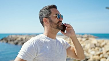 Genç İspanyol turist gülümseyerek kumsalda akıllı telefondan konuşuyor.