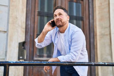 Kafkasyalı genç adam sokakta ciddi bir ifadeyle akıllı telefondan konuşuyor.