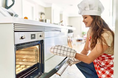 Genç, güzel, İspanyol bir kadın. Mutfakta kendine güvenen bir fırın açıyor.
