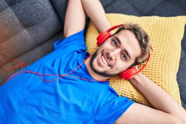 Young man listening to music lying on sofa at home