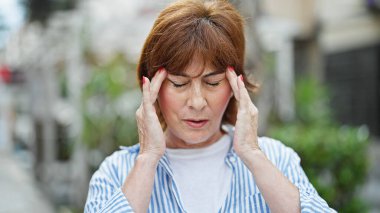 Sokakta baş ağrısı çeken orta yaşlı bir kadın.