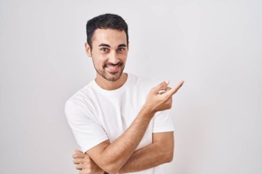 Beyaz arka planda duran yakışıklı İspanyol adam. Yüzünde kocaman bir gülümseme var. Elinle kameraya bakıyor.. 