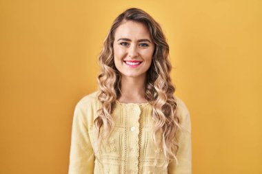 Yüzünde mutlu ve havalı bir gülümsemeyle sarı arka planda duran beyaz bir kadın. şanslı kişi. 