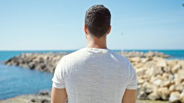 Genç İspanyol adam sahilde geri geri duruyor.