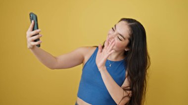 Genç ve güzel İspanyol kadın gülümsüyor. İzole edilmiş sarı arka planda kendine güvenen bir video kaydı var.