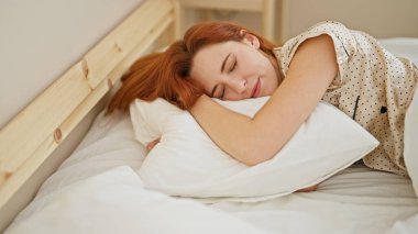 Genç kızıl saçlı kadın yatakta uzanıyor, yastığa sarılıyor, yatak odasında uyuyor.