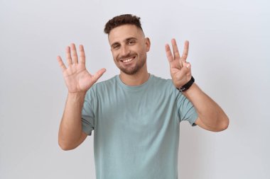 Hispanic man with beard standing over white background showing and pointing up with fingers number eight while smiling confident and happy. 