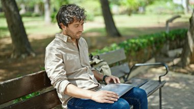 Genç İspanyol adam dizüstü bilgisayarı kapatıyor parkta rahatça oturuyor.