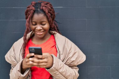 Siyah arka planda akıllı telefon kullanarak gülümseyen Afrikalı Amerikalı kadın.
