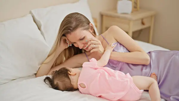 Mother and daughter lying on bed smiling at bedroom
