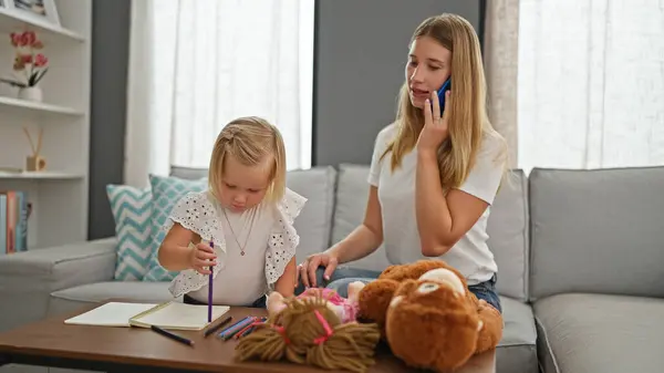 Relaxed mother-daughter bond, caucasian mum and little girl draw on notebook, engaging in serious talk over smartphone at home