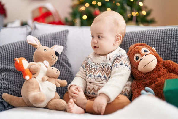 스러운 아기가 소파에 앉아서 크리스마스 옆에서 자랑스럽게 있습니다 — 스톡 사진