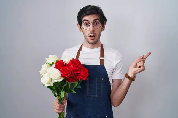 Joven Hombre Hispano Sosteniendo Ramo Rosas Blancas Rojas Sorprendido Señalando —  Fotos de Stock