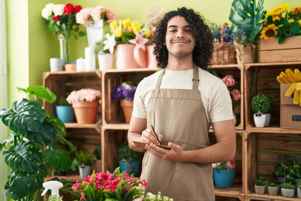 Young latin man florist smiling confident writing on envelope letter at flower shop