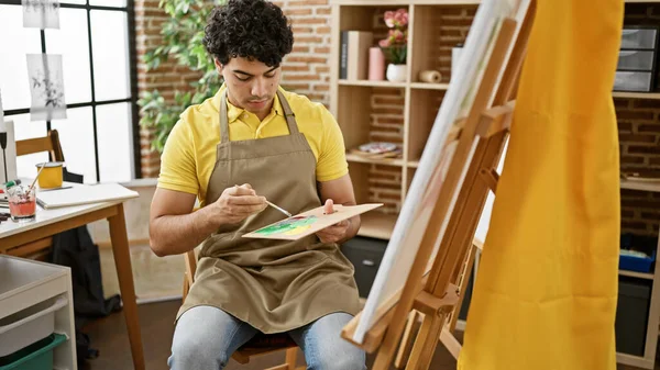 年轻的拉丁艺术家坐在艺术工作室的椅子上画画 — 图库照片